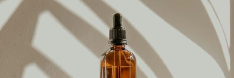 Amber glass dropper bottle of beard care oil on a windowsill, part of a Grooming and Shaving routine