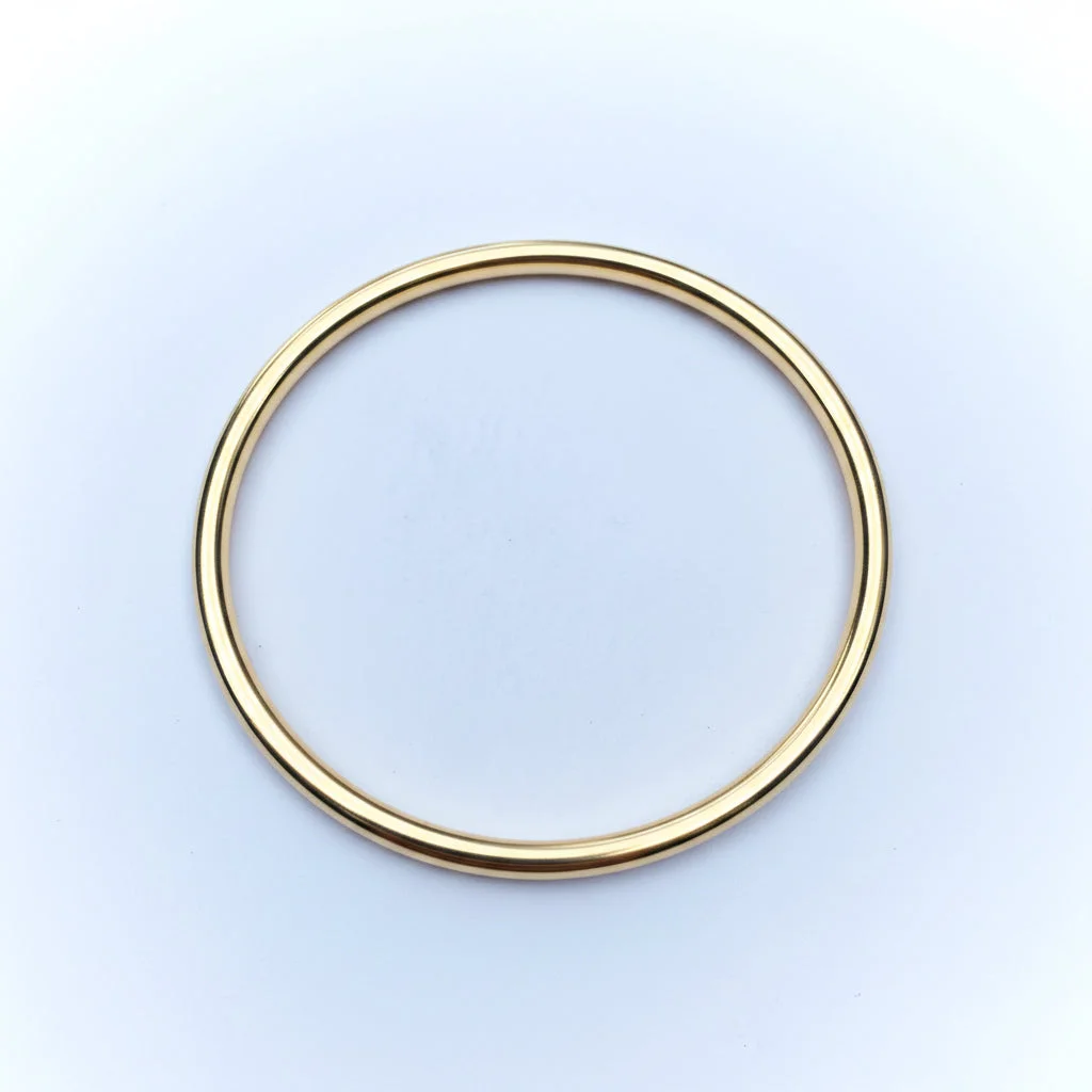 A simple polished metal bangle bracelet, appearing brass-toned, shown against a light background.