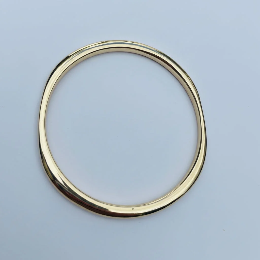 A polished brass metal bangle bracelet with a smooth, oval profile, displayed on a solid light blue background.