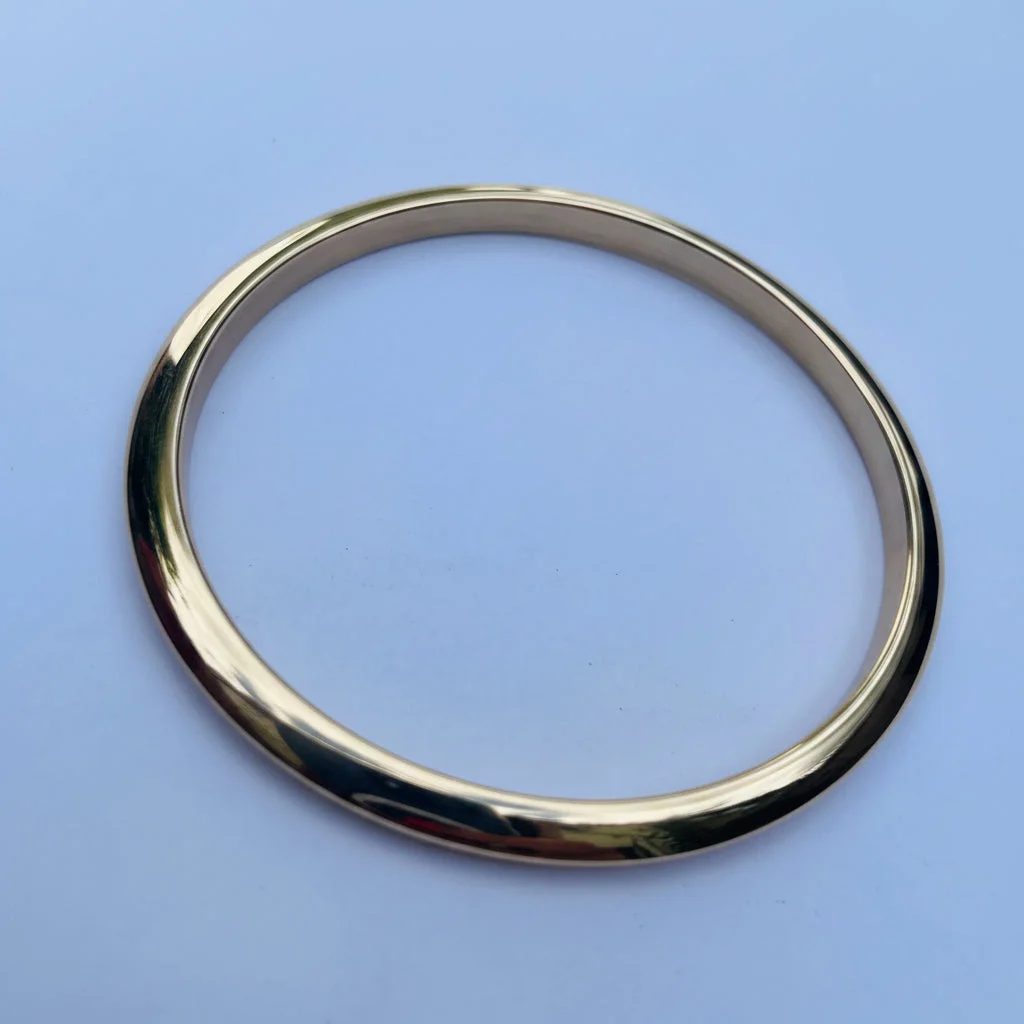 A polished gold-colored metal bangle bracelet shown on a light background.