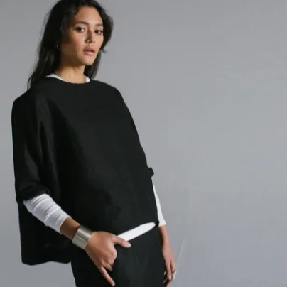 Person wearing a black poncho over a white shirt on a gray background