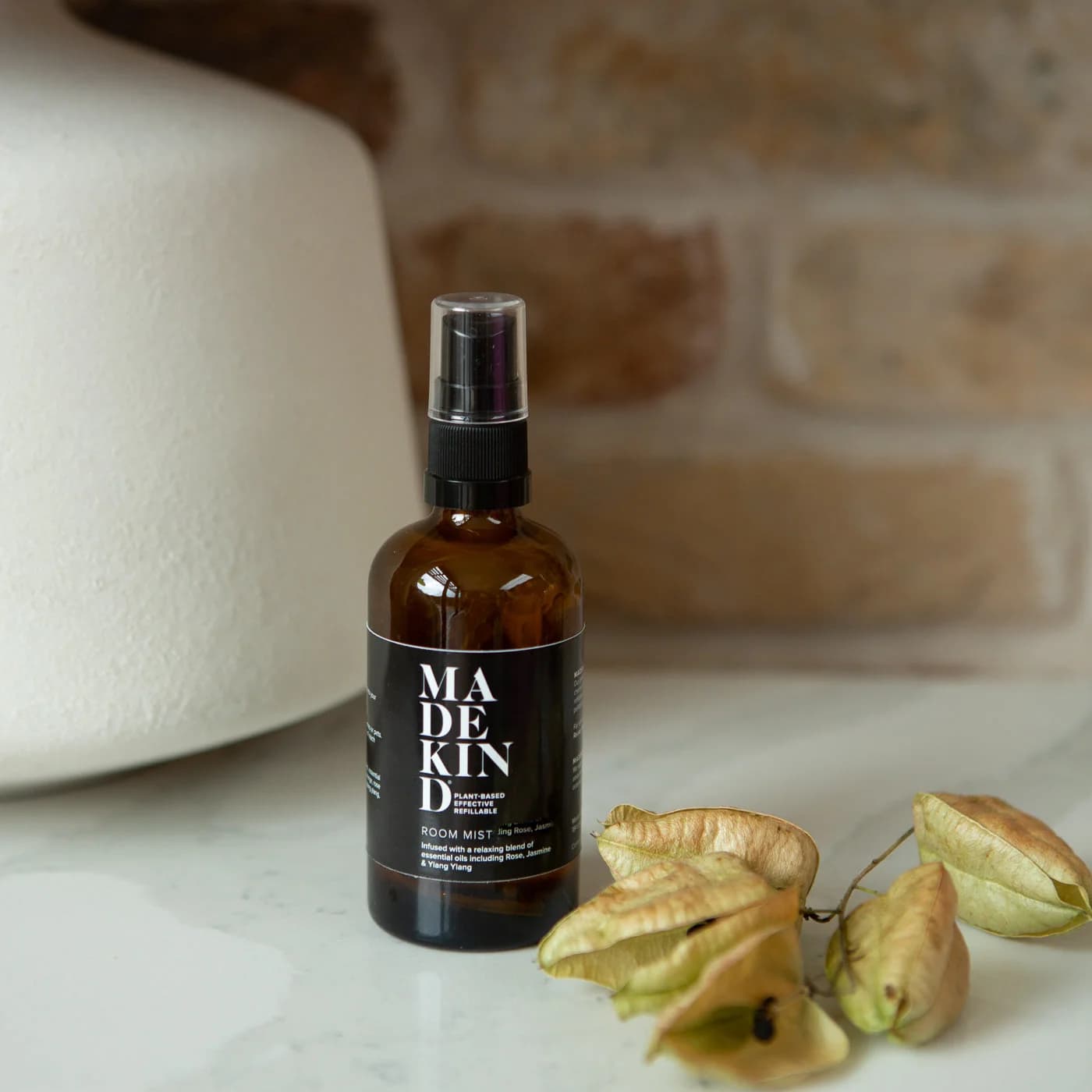A natural room mist spray bottle labeled 'MADEKIND' with a focus blend of Lavender, Rosemary, and Peppermint, placed on a surface alongside some dried plants.