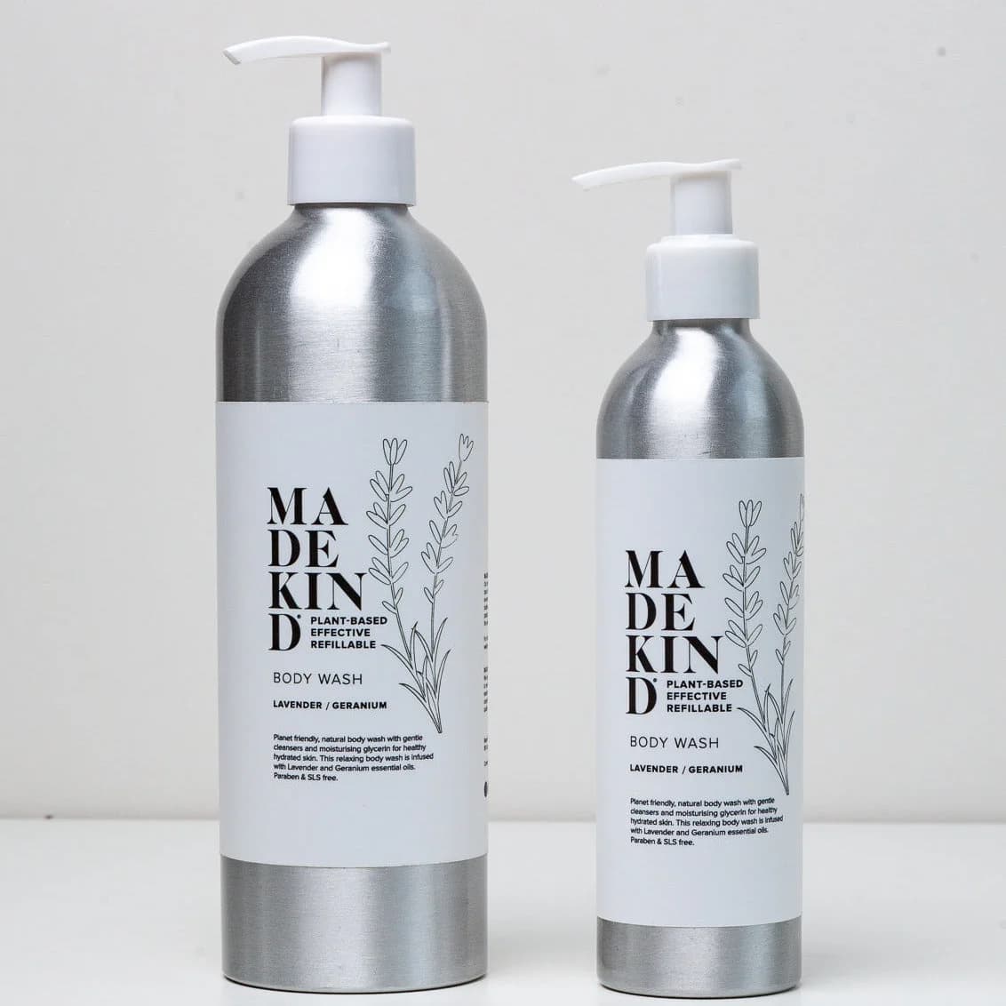 Two silver pump bottles of MADE KIND body wash with white labels, one larger and one smaller, standing on a white surface against a light gray background.