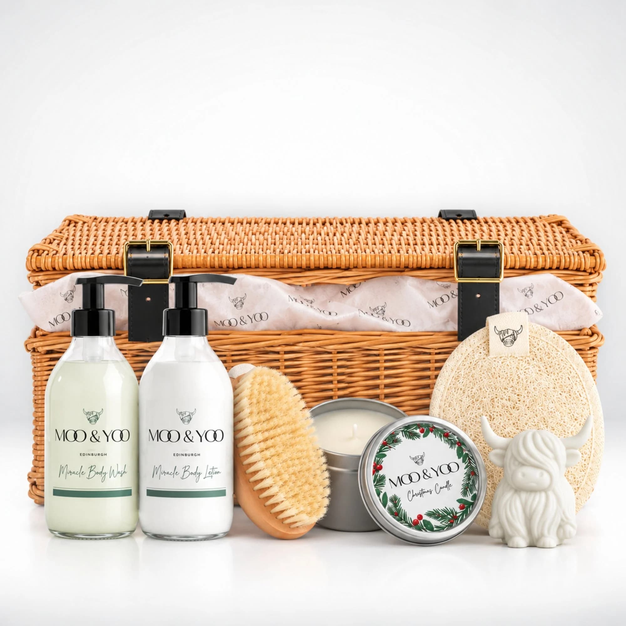 Moo & Yoo Luxury Body Care Christmas Hamper featuring Miracle Body Wash, Body Lotion, sisal body brush, body buffer, Highland cow soap and festive candle in a wicker basket with branded tissue paper.