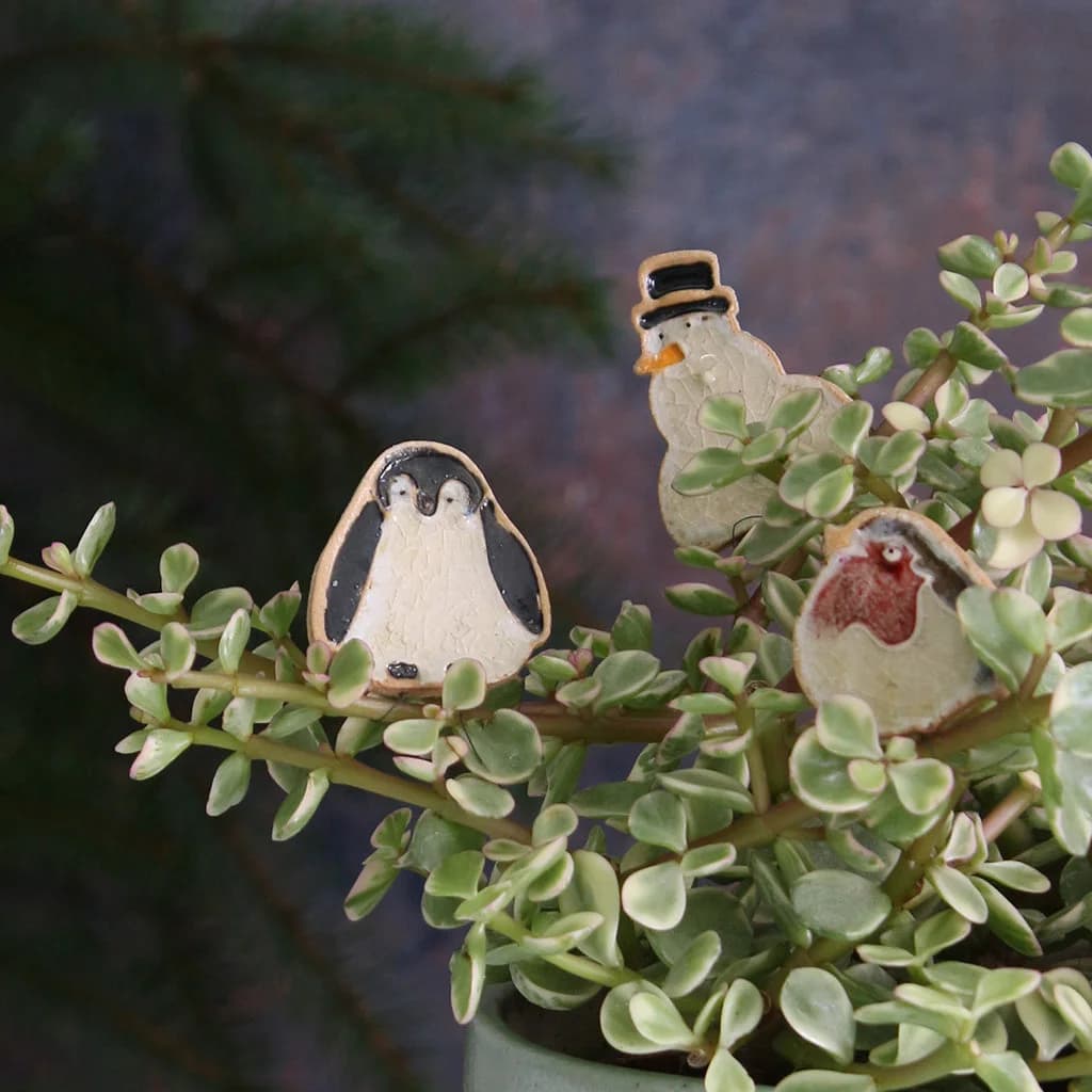 Three small ceramic figurines of a penguin, a snowman, and a bird on a plant with a blurred background.