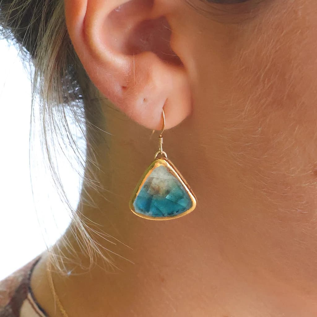 A women wearing a teardrop earring made from ceramic and teal glass with gold detailing.