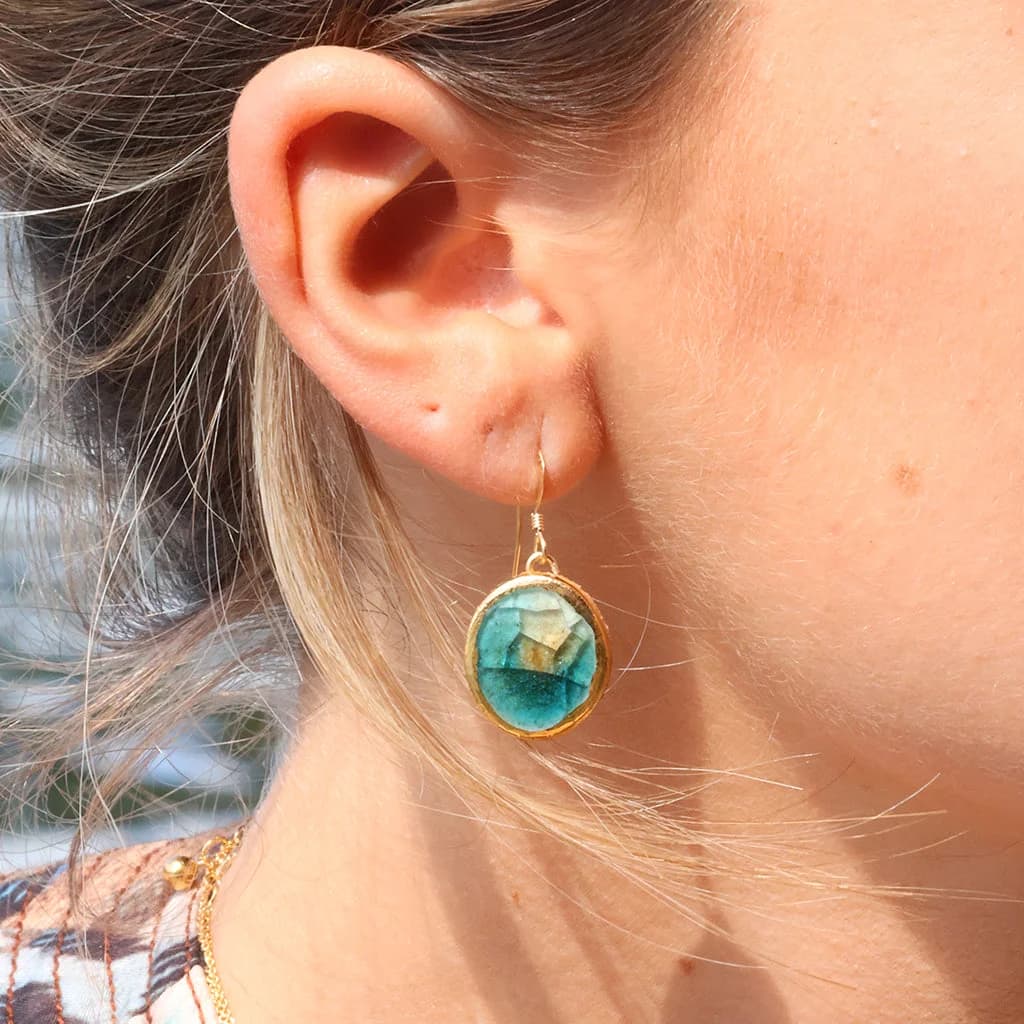 A women wearing a teal drop earring made from ceramic and glass with gold detailing.